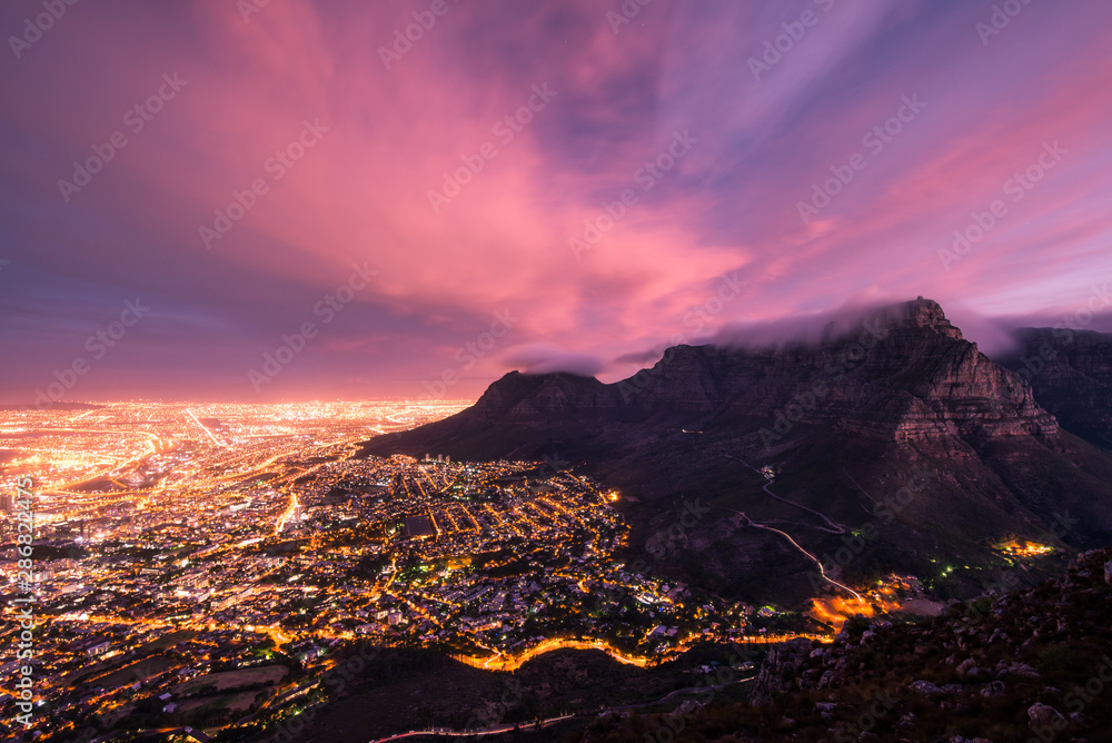 Fototapeta premium Moody Table Mountain after sunset with city lights as seen from Lions Head.