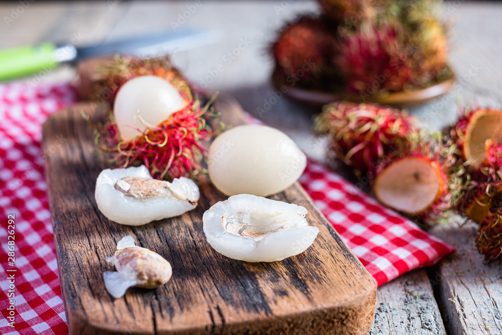 Mix of whole and peeled rambutan on wooden cutting board and table. Rambutan is an exotic fruits from tropical countries. Mix of whole and peeled rambutan on wooden cutting board and table. Rambutan is an exotic fruits from tropical countries.