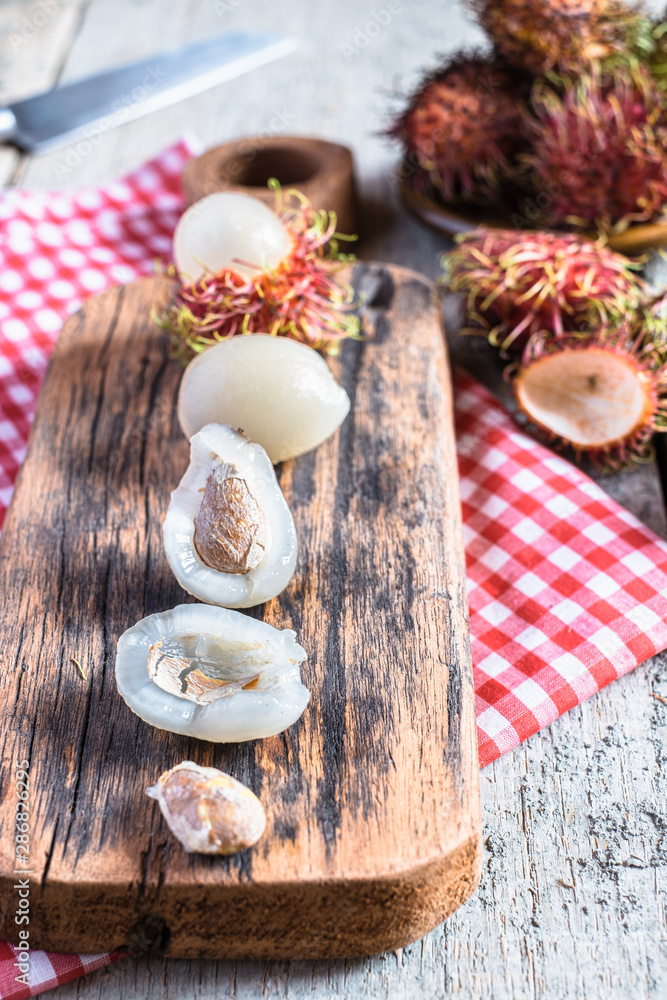 Mix of whole and peeled rambutan on wooden cutting board and table. Rambutan is an exotic fruits from tropical countries. Mix of whole and peeled rambutan on wooden cutting board and table. Rambutan is an exotic fruits from tropical countries.