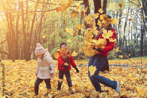 happy family walking in sunny park and throws orange maple leaves. mother with kids enjoying autumn weather outdoors