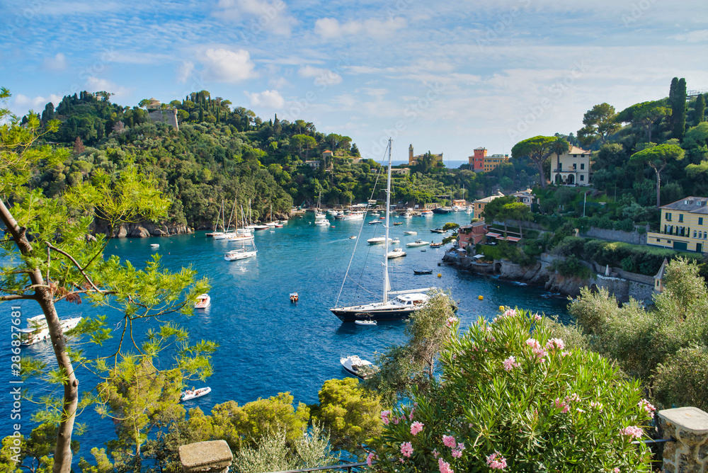 Portofino, Italy - AUGUST 15, 2019: Beautiful harbor in the Italian Riviera, houses on a cliff, boats and a yacht on water / a popular resort in Europe