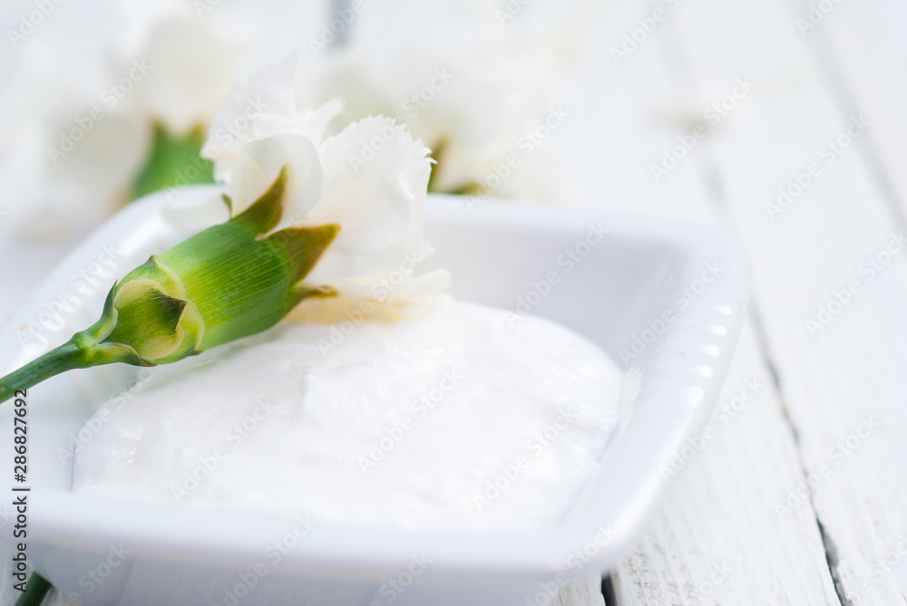 cosmetic cream and white carnation flowers on bright wooden table