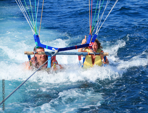 Happy couple parasailing on beach in summer. two people under parachute lowered into sea for fun