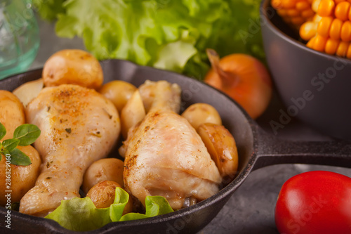 Roasted chicken legs with spices and herbs on the black pan.with vegetables on the background © zulfiska