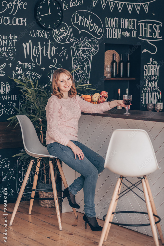 Fototapeta premium Young woman sitting on a chair near desk in the modern loft kitchen.