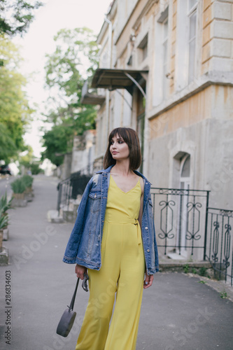 Woman in stylish yellow jumpsuit posing on city streets. © polinaloves