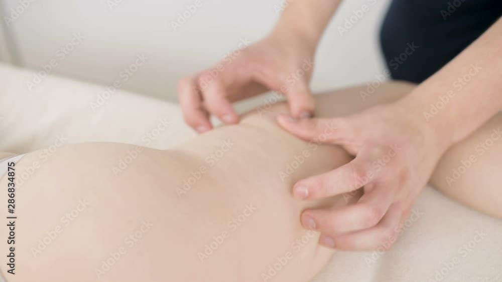 Close-up of a male physiotherapist doing a light massage to warm up the hips and buttocks of a young woman in a professional spa salon next to a sprig of cotton. 4K massage body care concept Close-up of a male physiotherapist doing a light massage to warm up the hips and buttocks of a young woman in a professional spa salon next to a sprig of cotton. 4K massage body care concept