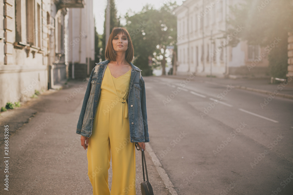 Woman in stylish yellow jumpsuit posing on city streets.