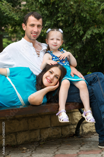 Family sitting on a bench in park. Woman pregnant. Happy family life concept.