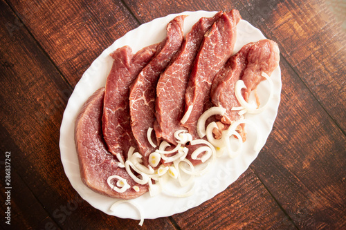 Juicy beautiful red meat with spices and onions on a white plate. Pepper and spicy meat marinated according to traditional recipes. Proper nutrition and natural food. Top view, wooden background. photo