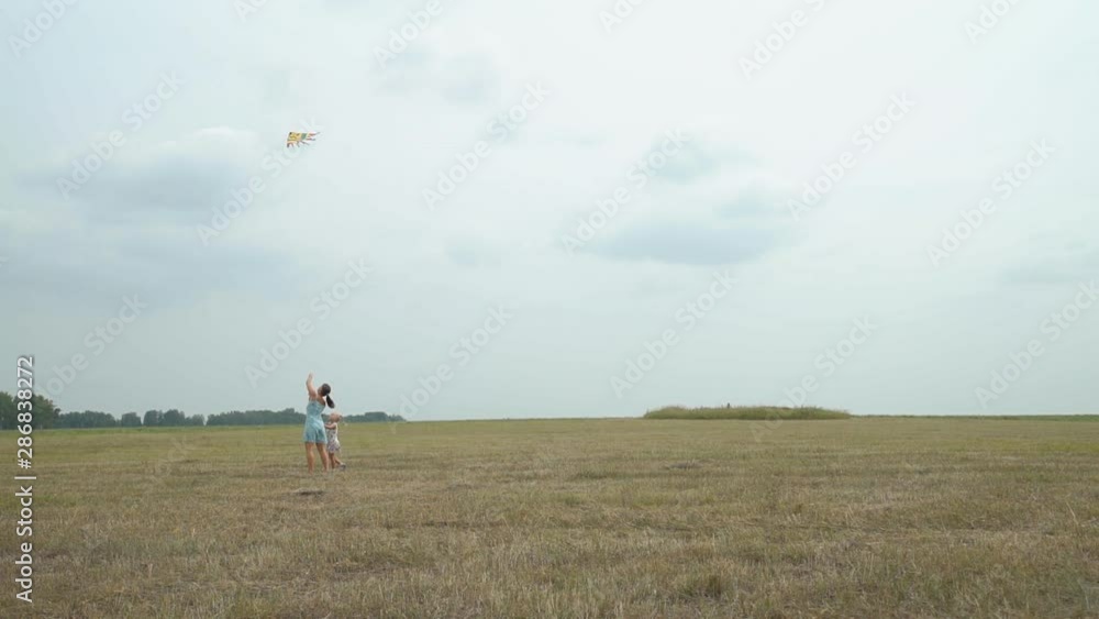 Young Mother and her Little Daughter Launching a Colorful Kite in the Field. Freedom and Family Holiday Concept Young Mother and her Little Daughter Launching a Colorful Kite in the Field. Freedom and Family Holiday Concept