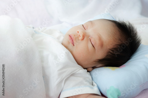 Closeup head shot of newborn baby boy sleeping in bed and lying in white clothes on white.