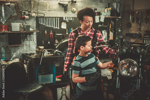 African american woman mechanic and boy helper repairing a motorcycle in a workshop