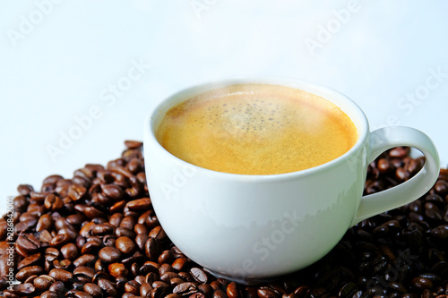 White coffee cup filled with hot coffee and smoke surrounded by roasted coffee beans isolate on white background.