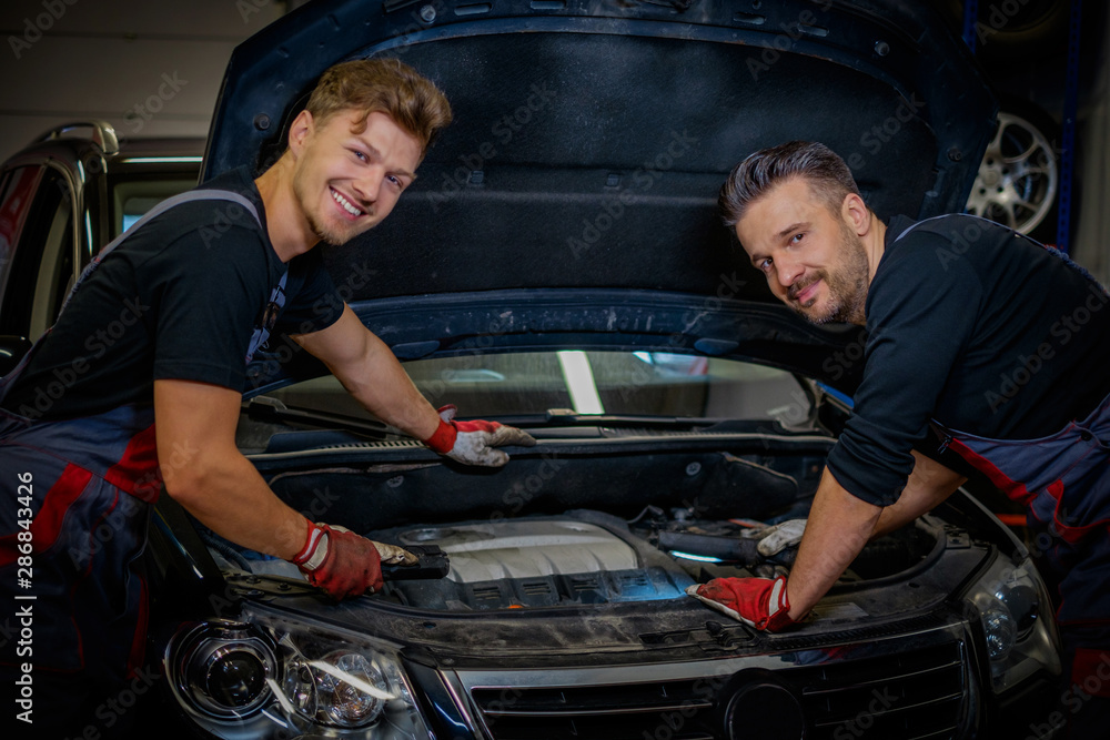 Car mechanics checking under hood in a workshop Car mechanics checking under hood in a workshop