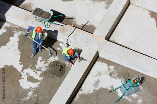 Uniformed workers clean sand on a construction site, top view.