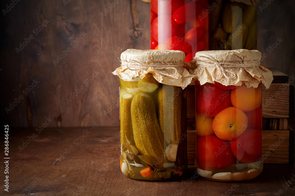 Homemade pickled tomato and cucumber in glass jars on an wooden rustic background