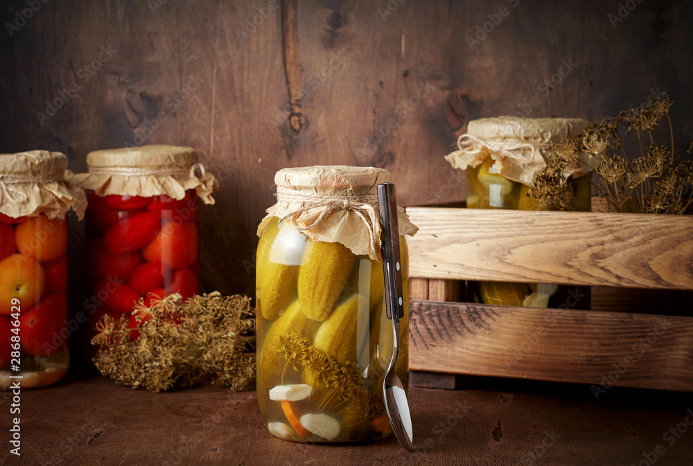 Homemade pickled tomato and cucumber in glass jars in wooden rustic box
