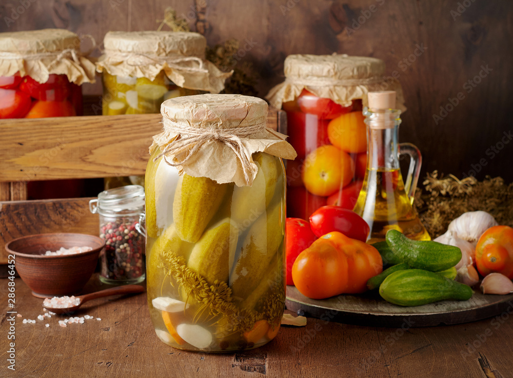 Homemade pickled tomato and cucumber in glass jars on an wooden rustic background