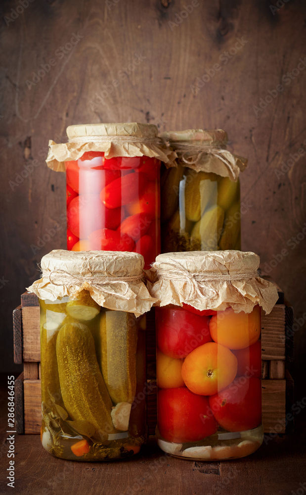 Homemade pickled tomato and cucumber in glass jars on an wooden rustic background