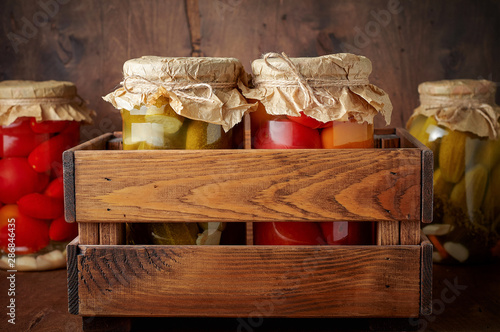 Homemade pickled tomato and cucumber in glass jars in wooden rustic box