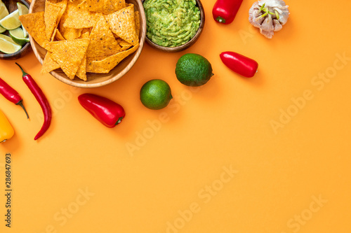 top view of crispy nachos, guacamole and spices on orange background with copy space