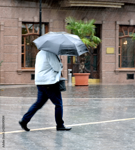 Man with umbrella walking down the street in rainy day in motion blur