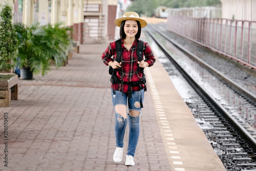 Young beautiful female travel photographer enjoys taking photo during her trip at railway station. Asian woman travel with camera having fun making pictures while waiting for train.