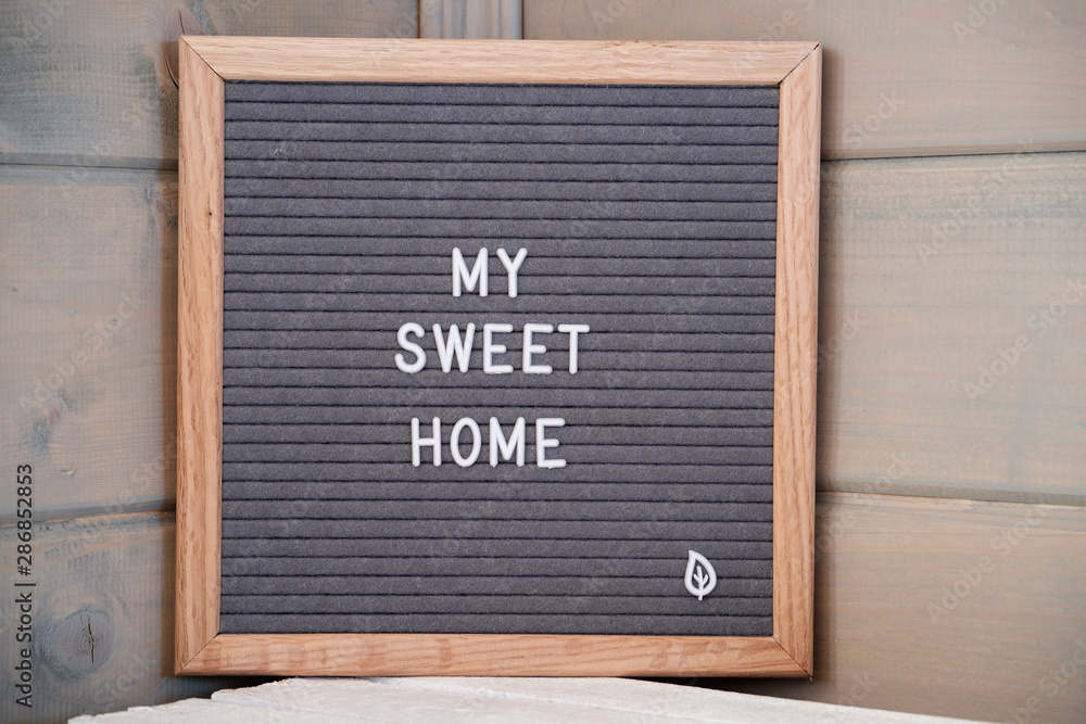 Grey lettering Board with felt coating in wooden frame with English text my sweet home in corner of wooden house