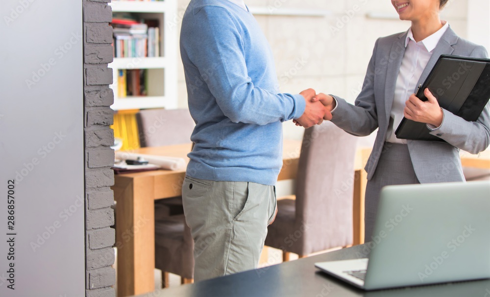 Smiling young saleswoman shaking hands with mature man in apartment Smiling young saleswoman shaking hands with mature man in apartment