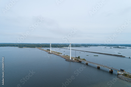 Three spinning wind turbines near a river in a countryside area. A car passes on the nearby road.  © raland