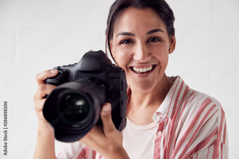 Portrait Of Smiling Female Photographer With Camera Against White Studio Wall Portrait Of Smiling Female Photographer With Camera Against White Studio Wall