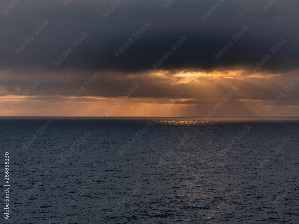Dark and moody sky over the ocean, Sun shines through the clouds, Orange and dark color.