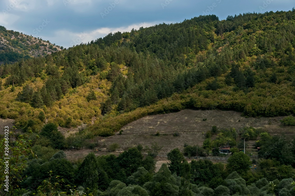 Amazing autumn view of glade, field, peak, deciduous forest, trees and small village in Sredna gora mountain, Bulgaria  