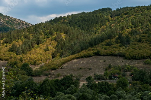 Amazing autumn view of glade, field, peak, deciduous forest, trees and small village in Sredna gora mountain, Bulgaria 