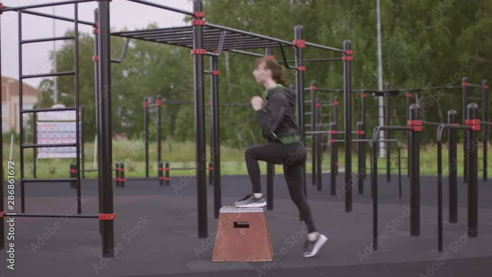 Sportive woman doing reverse lunge with rear leg raise with box while training at outdoor fitness court Sportive woman doing reverse lunge with rear leg raise with box while training at outdoor fitness court