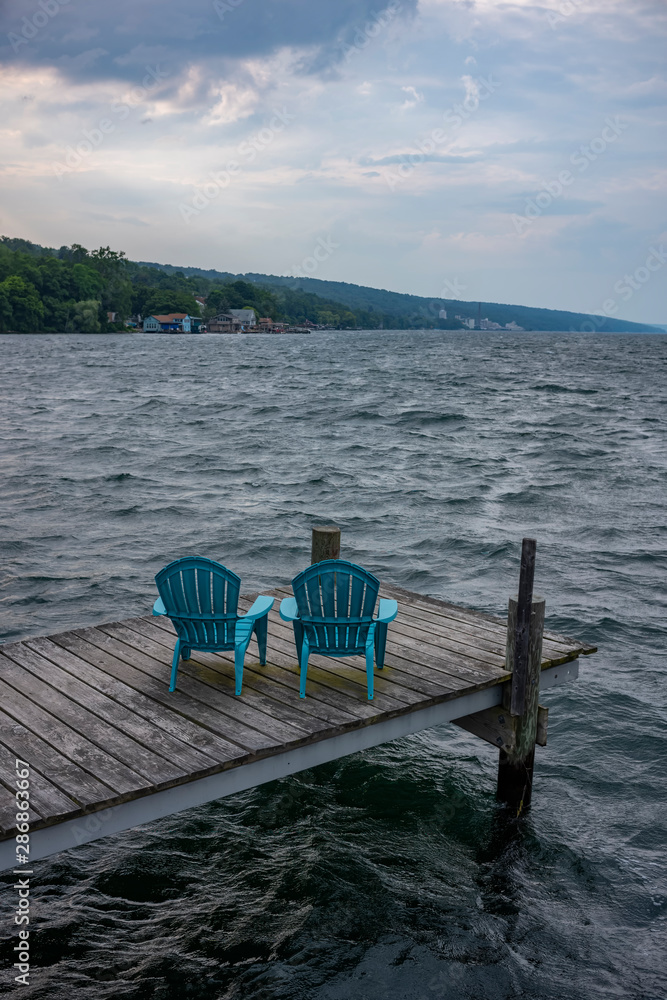 Φωτογραφία Rough waters, crash into a pier with two plastic and blue Adirondack garden chairs, as a storm comes in over Seneca Lake at Watkins Glen in New York State