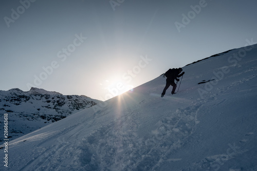 Man mountaineer climbing on snowy mountain in winter at sunset