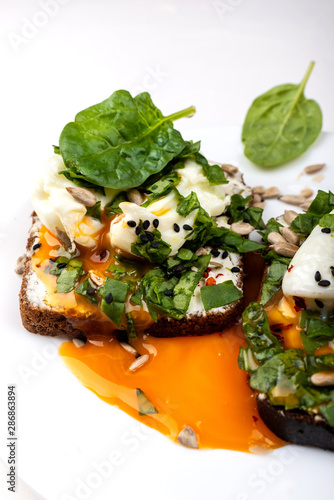 Sandwiches with poached eggs, cheese, spinach leaves, sesame seeds and seeds. Healthy breakfast or snack on the white background. Close-up.