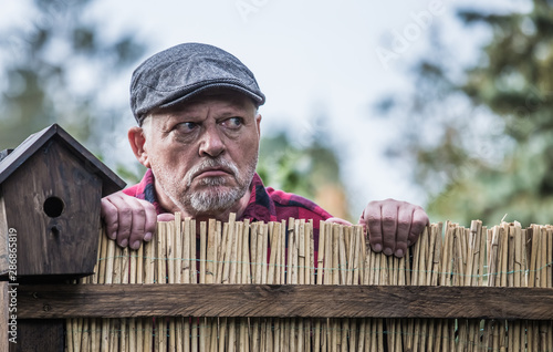 An evil, aggressive man watches his neighborhood over the garden fence. Concept dispute and aggression between people. photo