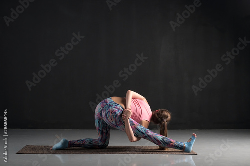 Sporty young woman doing stretching exercise, Ardha Hanumanasana or Half Monkey God Pose. Studio full length side view