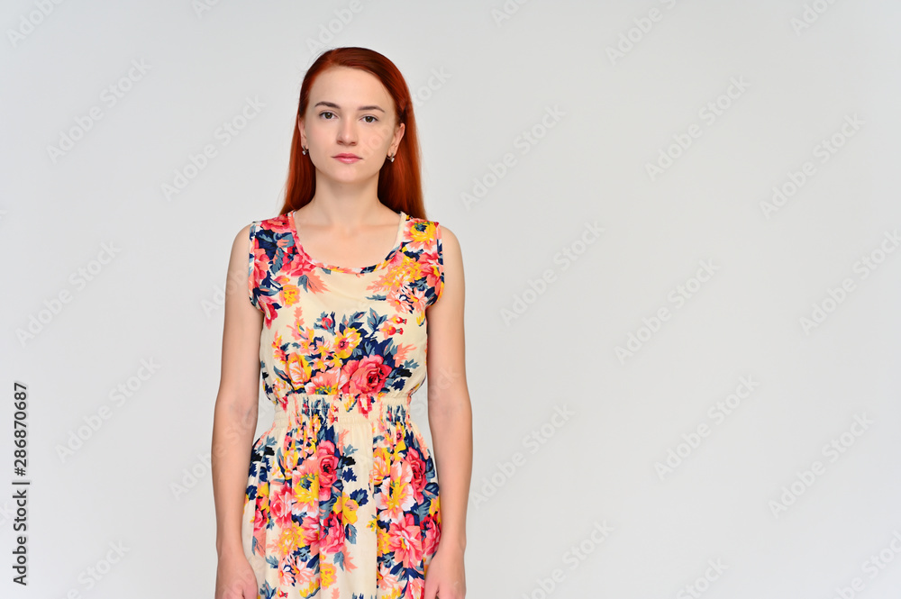 Portrait of a pretty red-haired girl, a happy young woman in a bright summer dress on a white background in the studio. Smiling, showing different emotions. Portrait of a pretty red-haired girl, a happy young woman in a bright summer dress on a white background in the studio. Smiling, showing different emotions.