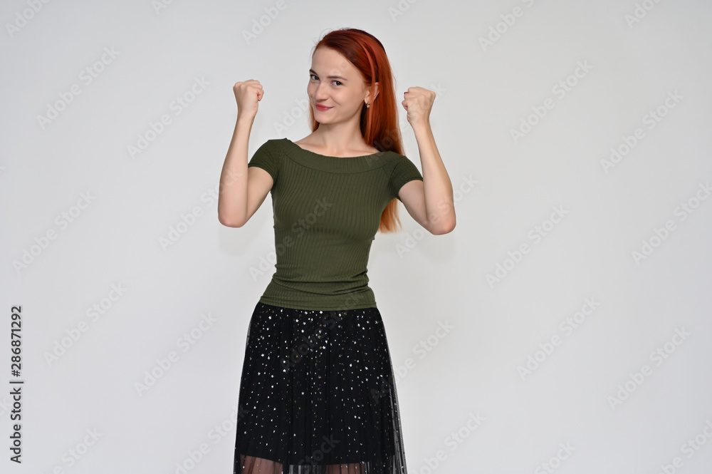 Portrait of a pretty red-haired girl, a happy young woman in a green T-shirt and black skirt on a white background in the studio. Smiling, showing different emotions. Portrait of a pretty red-haired girl, a happy young woman in a green T-shirt and black skirt on a white background in the studio. Smiling, showing different emotions.