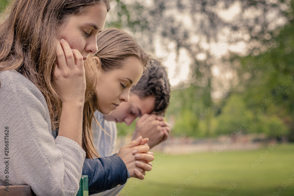 Christian worship and praise. Happy friends praying together in the park.