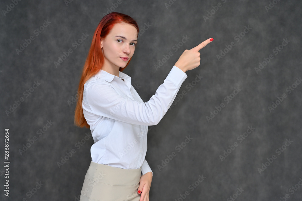 Portrait of a pretty red-haired girl, a happy young woman manager in a light business suit on a gray background in the studio. Smiling, showing different emotions. Portrait of a pretty red-haired girl, a happy young woman manager in a light business suit on a gray background in the studio. Smiling, showing different emotions.
