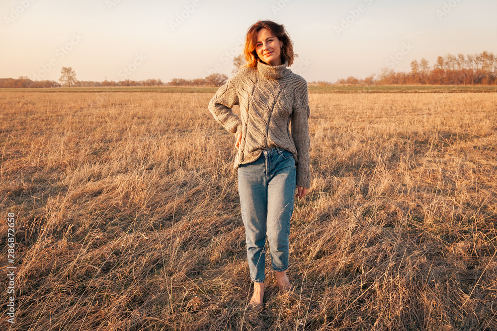 Posing woman in nature. Young woman in stylish clothes: knitted sweater and jeans posing against the backdrop of the forest, road and field. Photos on vacation in the fall Posing woman in nature. Young woman in stylish clothes: knitted sweater and jeans posing against the backdrop of the forest, road and field. Photos on vacation in the fall