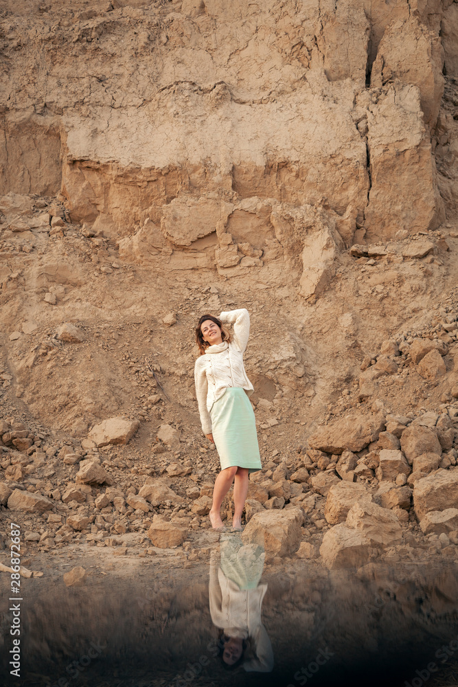 Posing woman in nature. Young woman in stylish clothes: a knitted sweater and a long skirt posing against the backdrop of a sand pit, reflected below. Interesting effects on photos using your phone