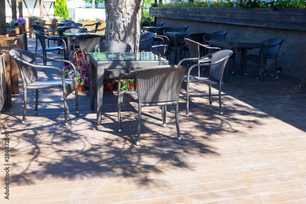 Naklejka premium Beautiful wicker tables and chairs made of artificial rattan are in the street cafe.
