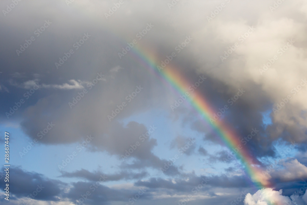 Rainbow and white clouds in blue sky after rain. Nature, travel concept, copy space