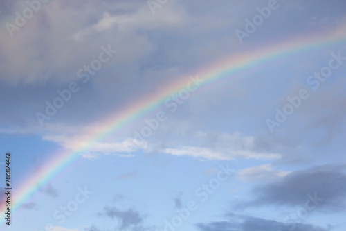 Rainbow and white clouds in blue sky after rain. Nature, travel concept, copy space